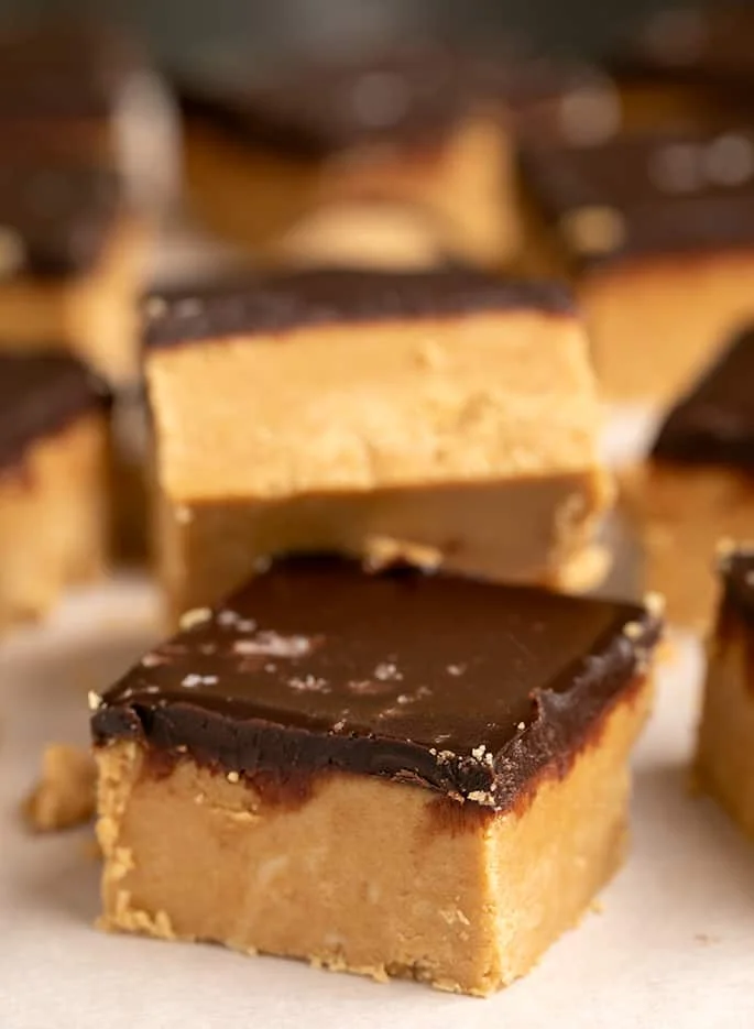 Squares of chocolate topped peanut butter bars piled together on white paper