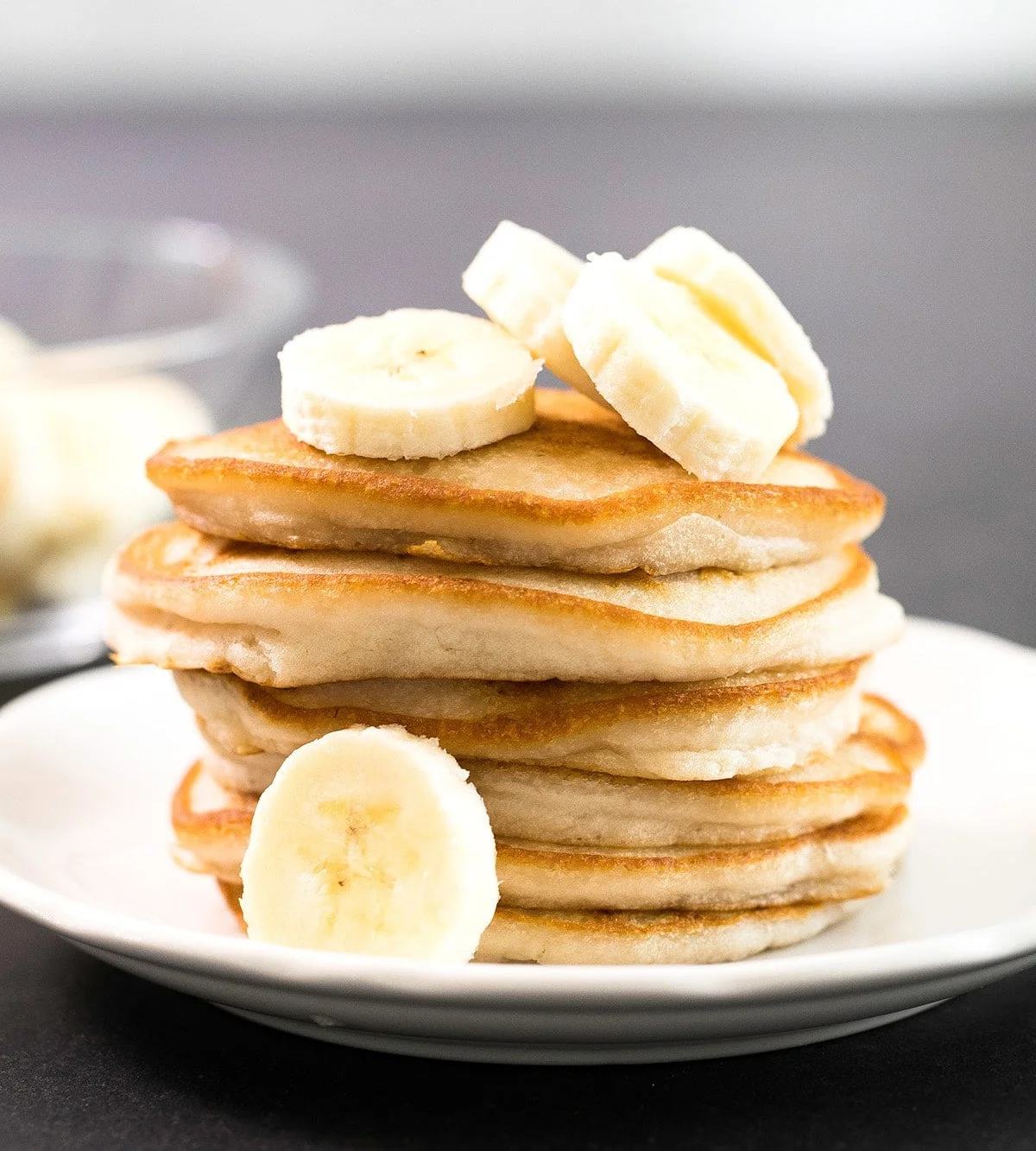 stack of 6 gluten free vegan pancake with golden brown edges on white plate with banana slices on the plate and on top of the stack