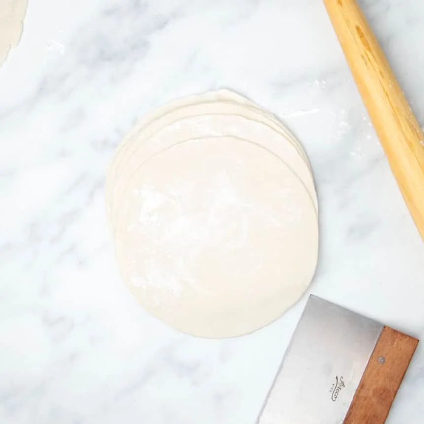 stack of 6 raw 8-inch round tortillas with white tapioca flour on top and metal bench scraper and rolling pin