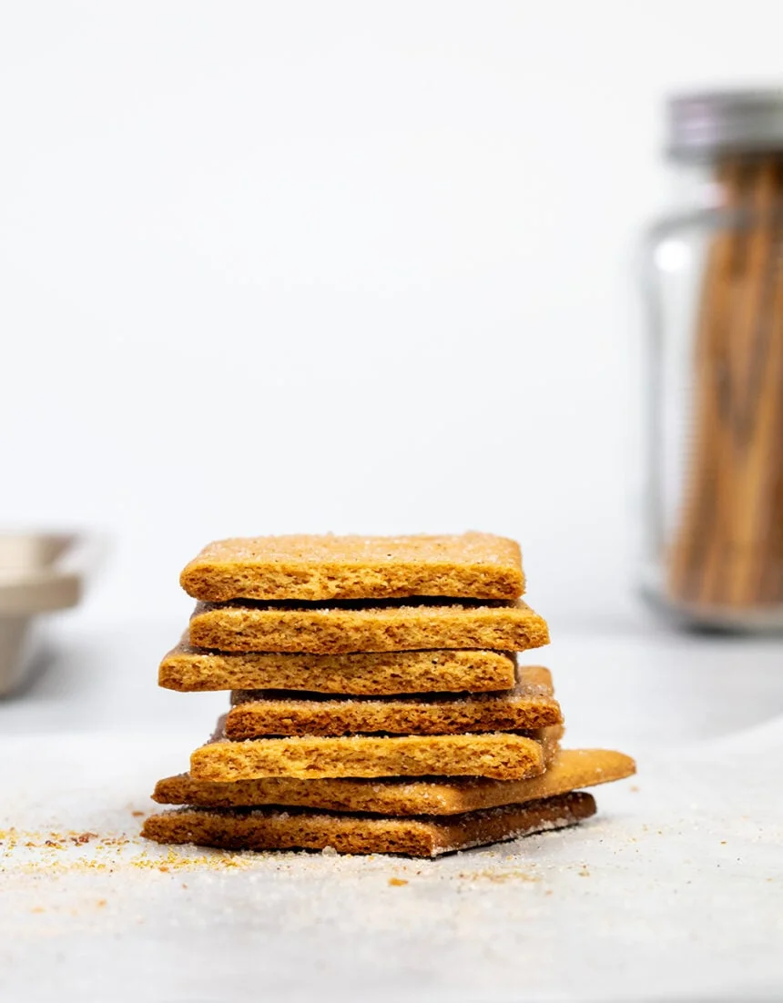 stack of 7 halves of light brown gluten free graham crackers with glass jar with more graham crackers in background