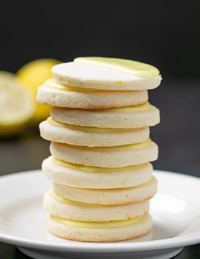 stack of 9 pale round cookies with yellow icing on top on small white plate on black surface