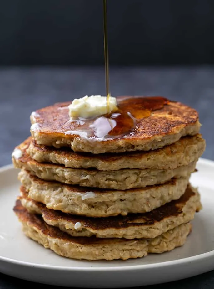 Stack of oatmeal pancakes with pat of butter and syrup being poured on top