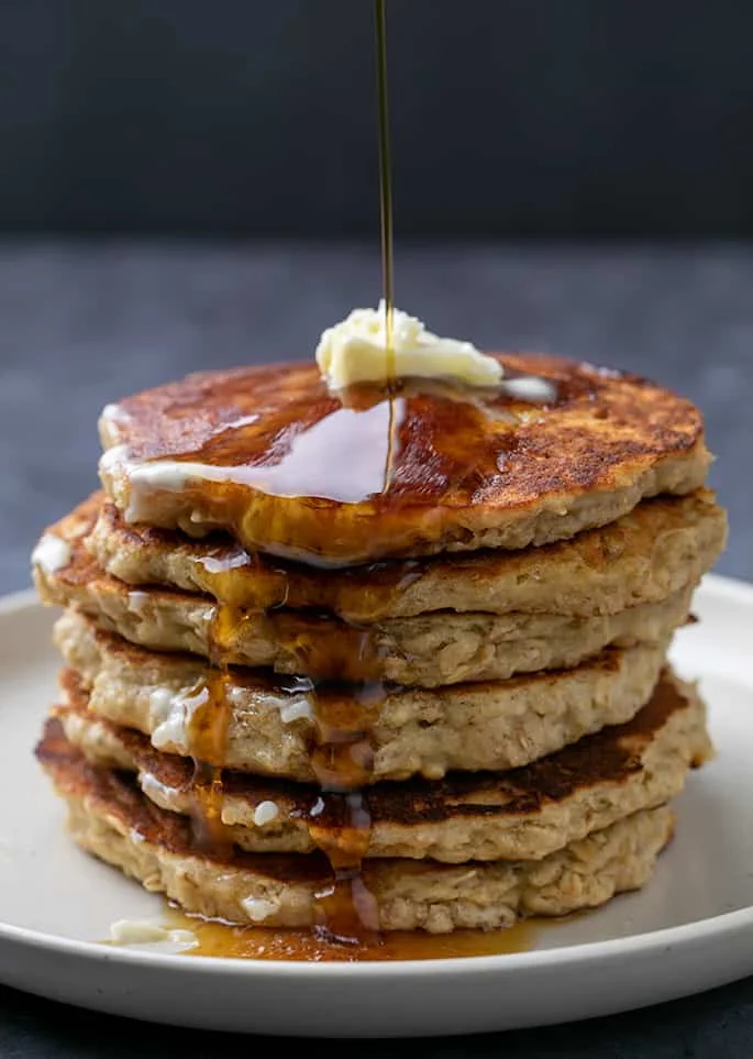 Stack of oatmeal pancakes with syrup pouring down the side