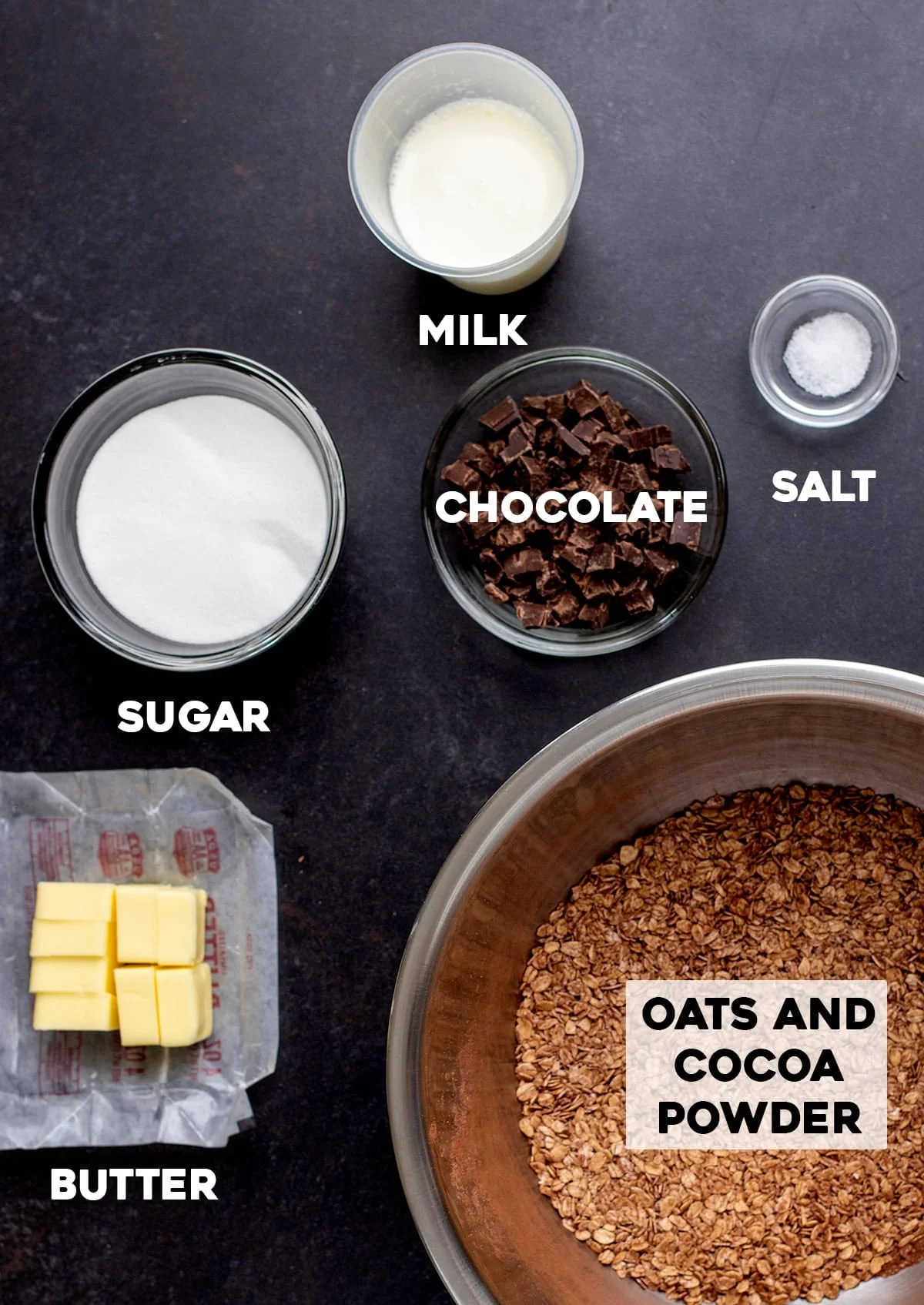 Sugar, milk, salt, chocolate, butter, gf oats and cocoa powder on black table