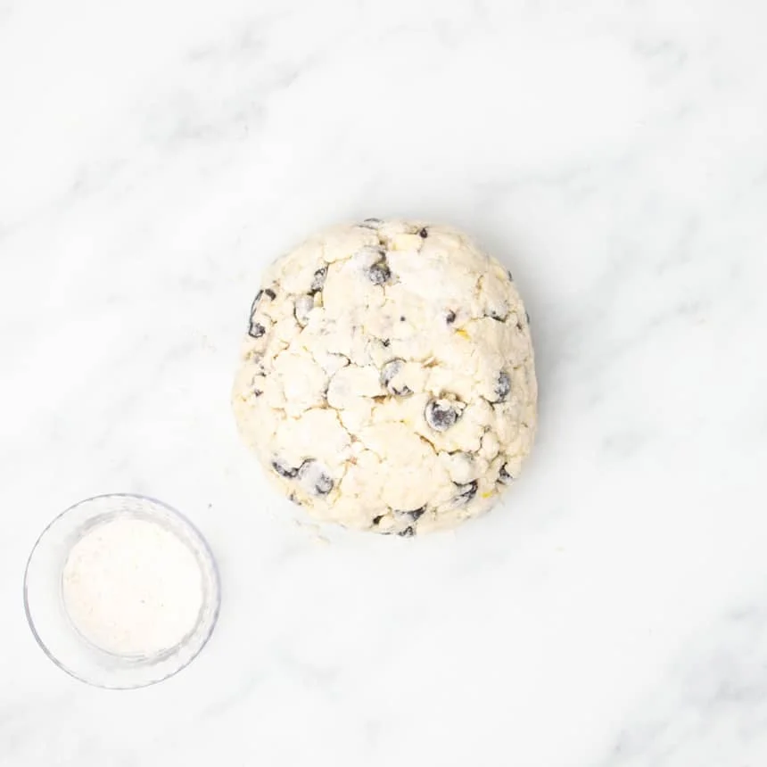 The dough shaped into a round disc on a marble surface next to a small glass bowl of extra gluten free flour.