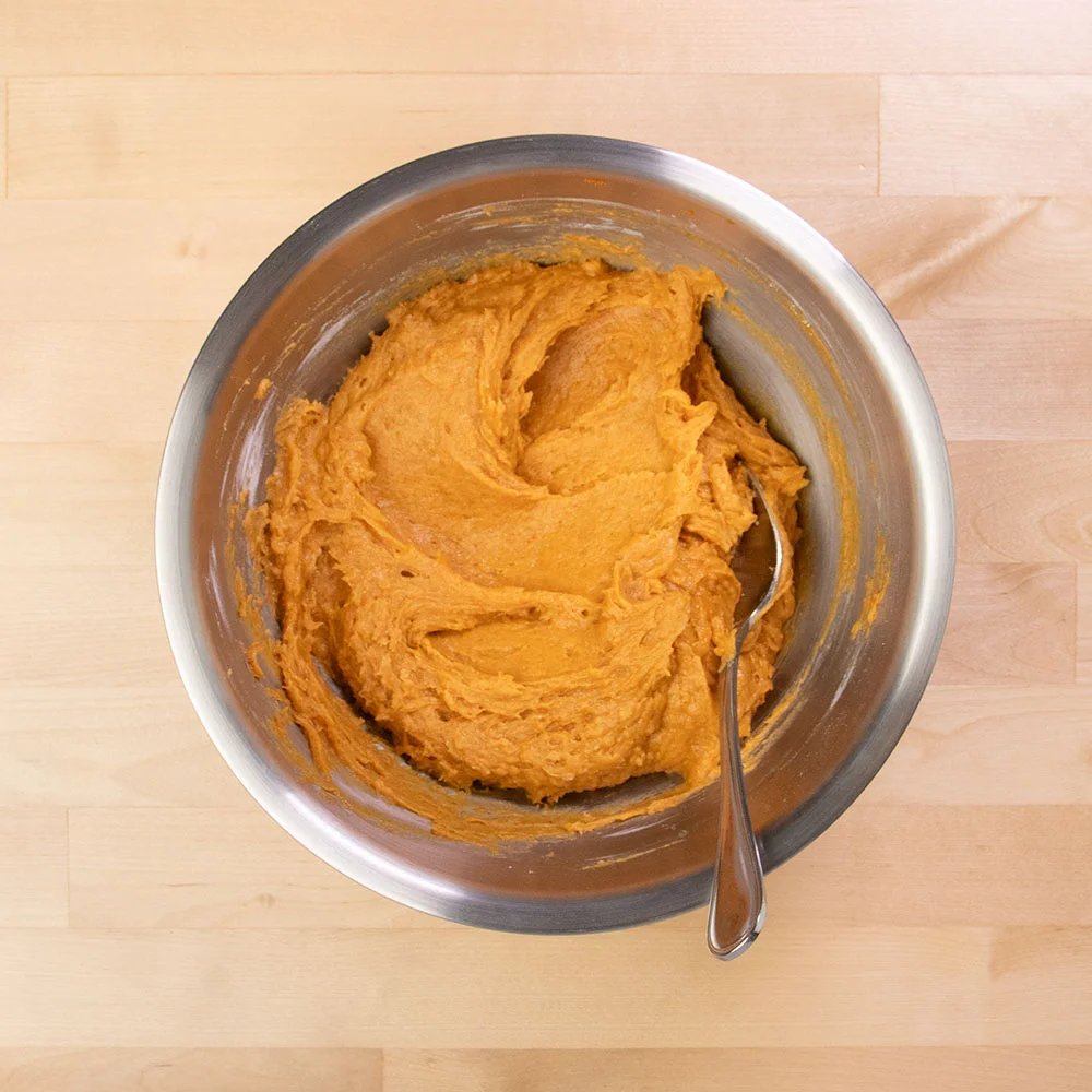 thick light orange muffin batter with metal mixing spoon on same bowl