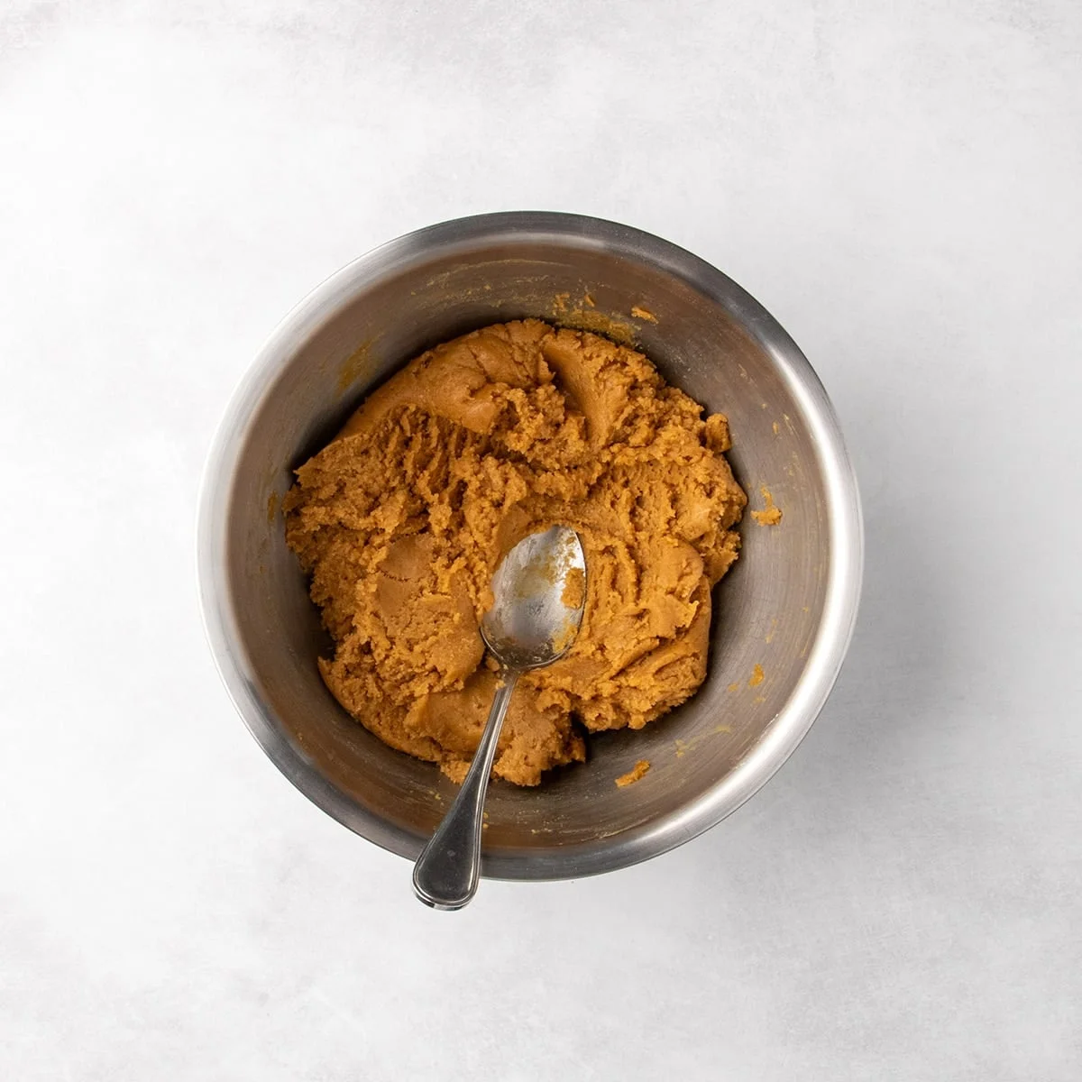 Thick peanut butter cookie dough in a metal mixing bowl with a spoon resting on top.