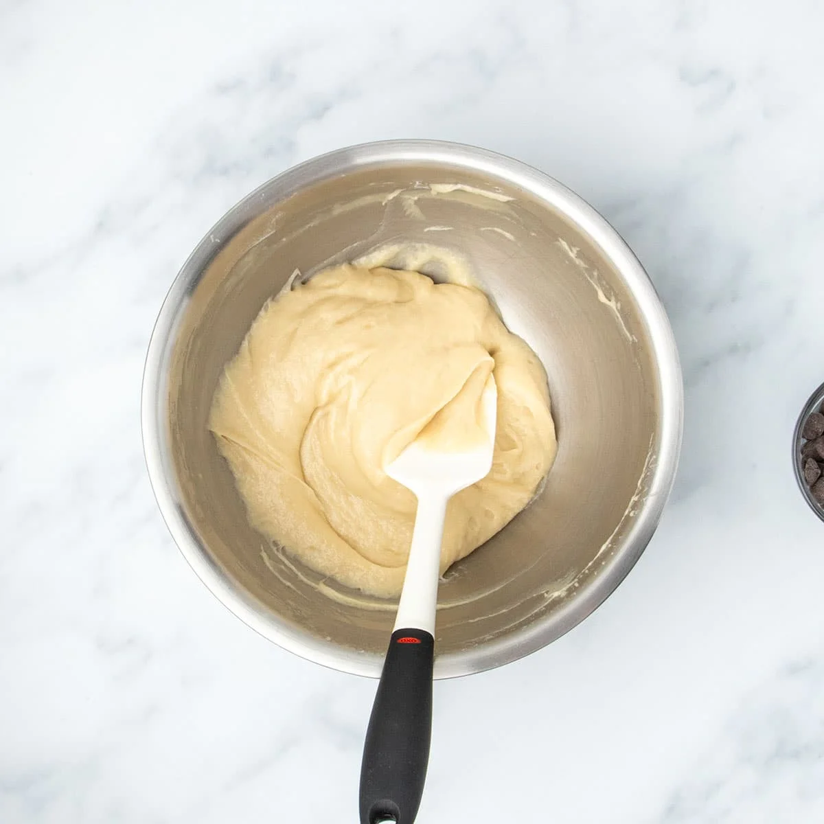 Thicker muffin batter after having rested being turned over with a silicone spatula before folding in chocolate chips.