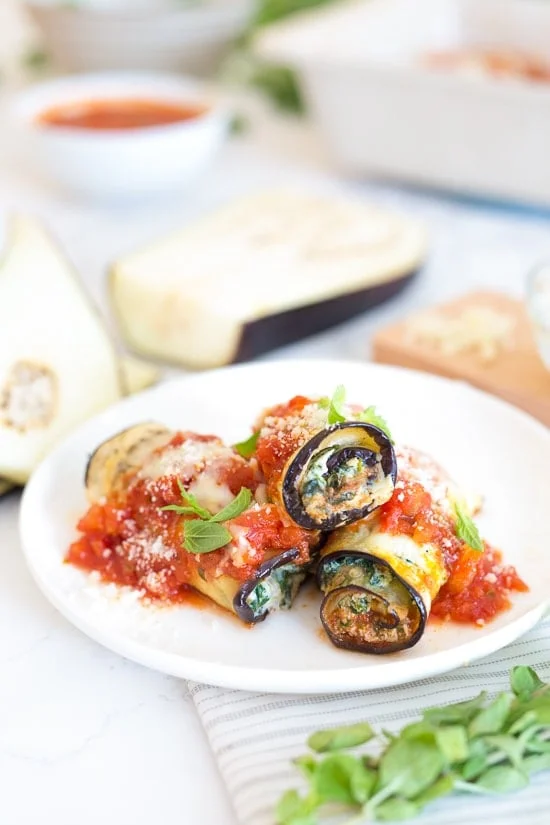 Three eggplant rollatini with sauce on a plate.