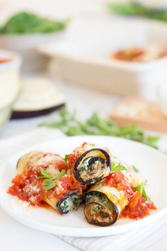 Three eggplant rollatini with sauce on a white plate.