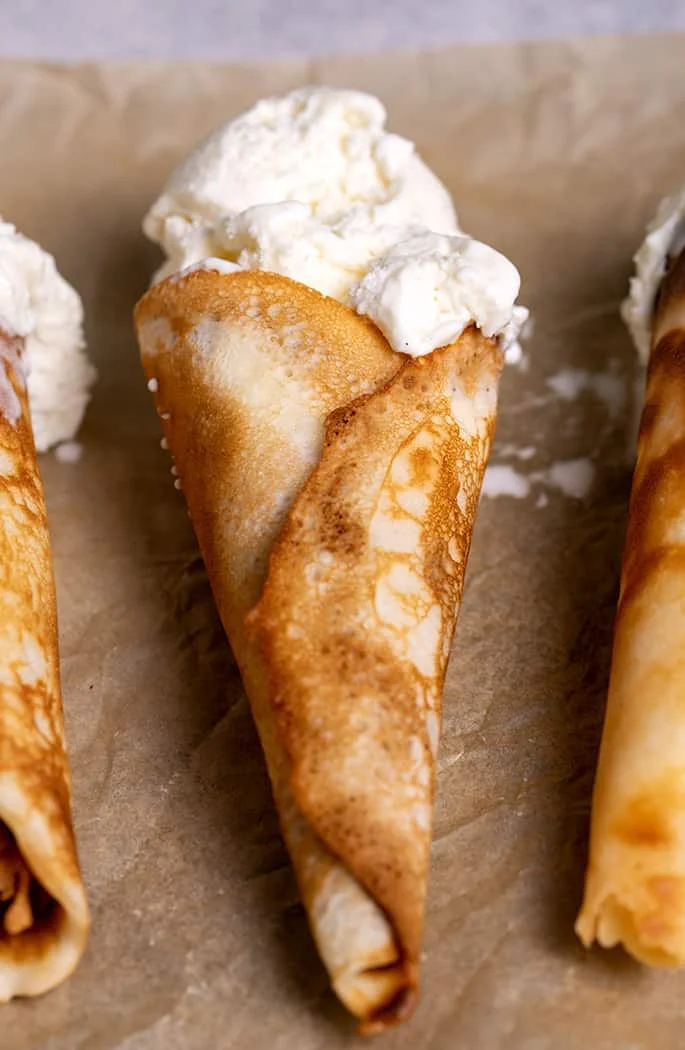 Three gluten free ice cream cones with vanilla ice cream flat on brown paper