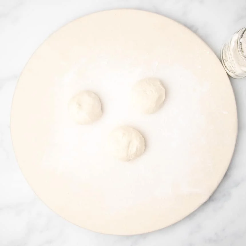 Three portions of dough shaped into smooth balls on a floured round surface.