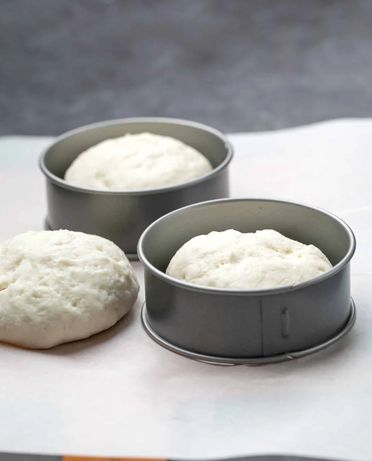 Three raw English muffins with 2 metal rings on white paper