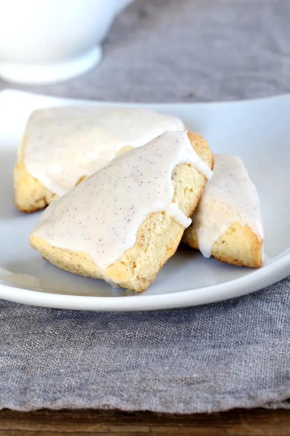 Three small vanilla scones with white icing on a plate.