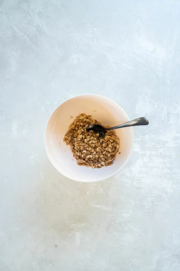 Topping ingredients for apple crisp combined in a white bowl with a spoon.