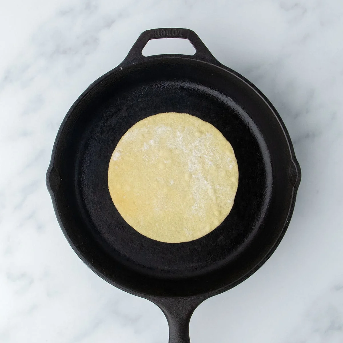 Tortilla placed in a hot cast iron skillet for cooking.