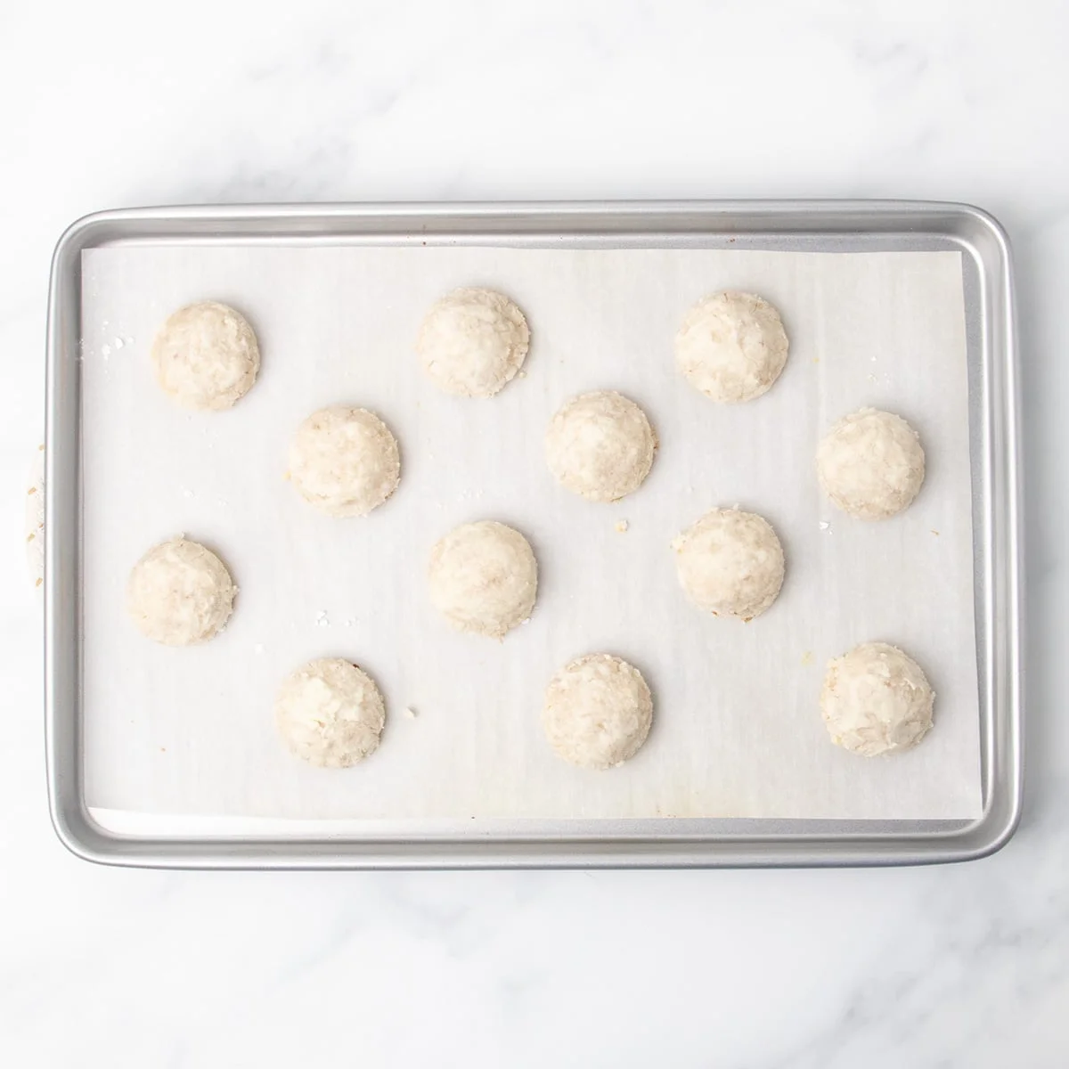 Twelve baked cookies that lightly crackled on top and pale in color on a parchment-lined baking sheet.