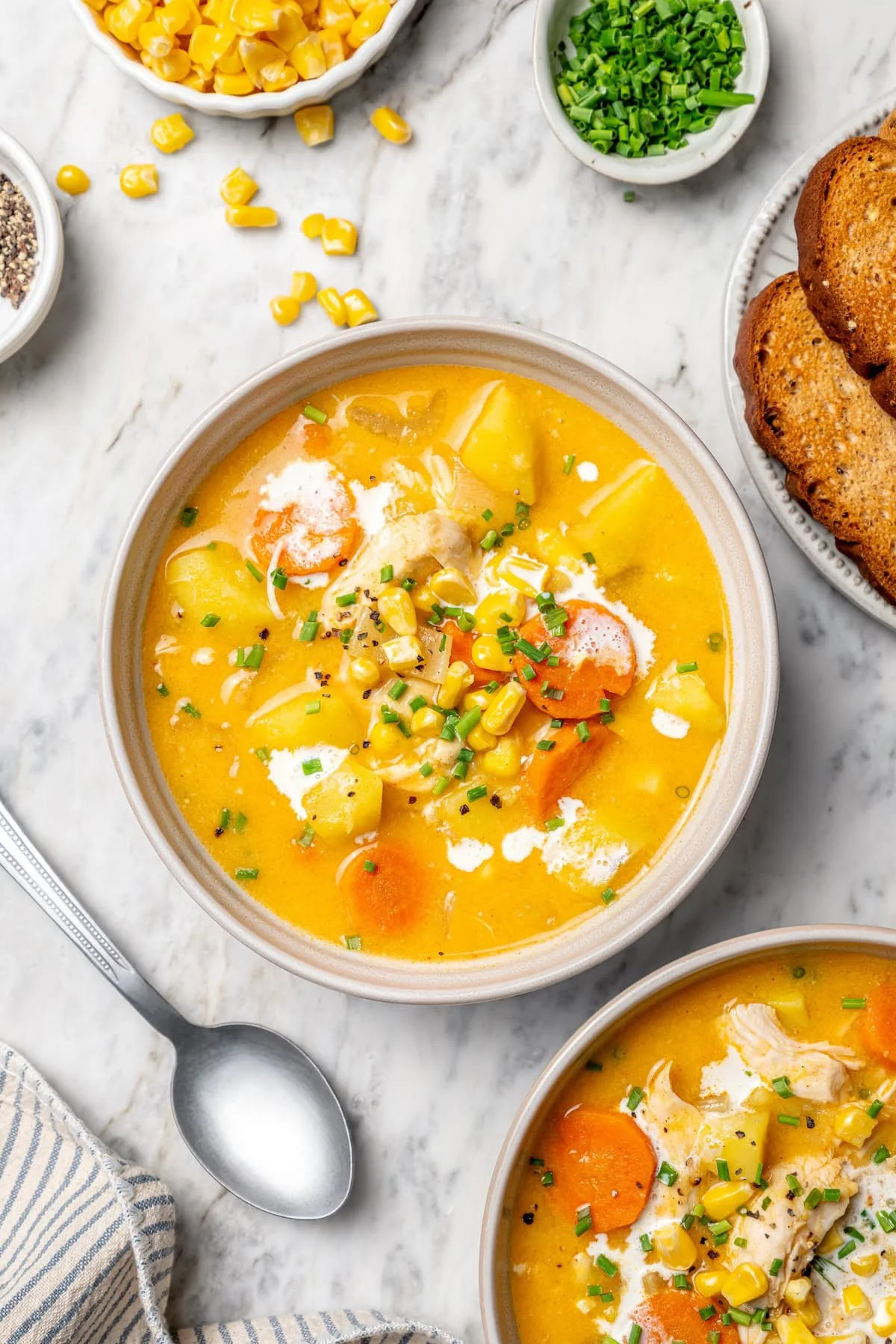 Two bowls of creamy chicken corn chowder on marble tabletop.