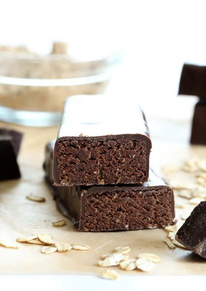 Two brown chocolate-coated cake-like bars with the ends cut off on brown paper with scattered oats