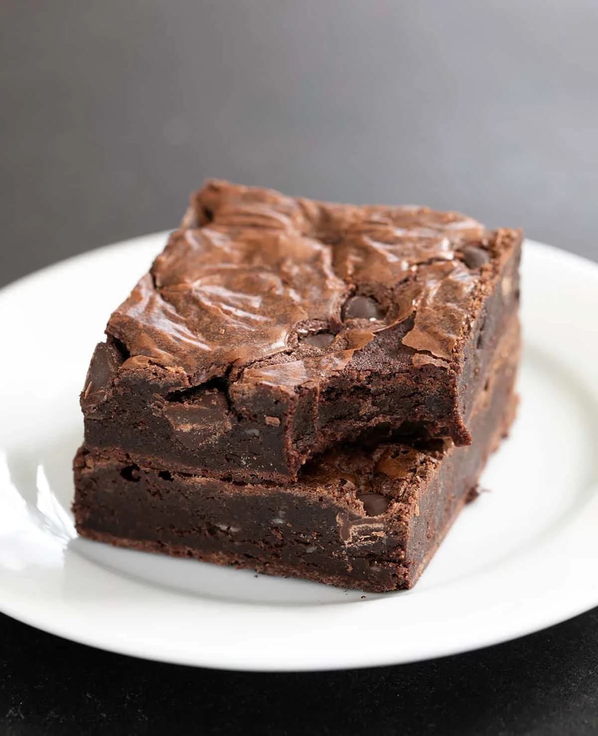 Two flourless brownies on a small white plate, in a stack (one with a bite taken)