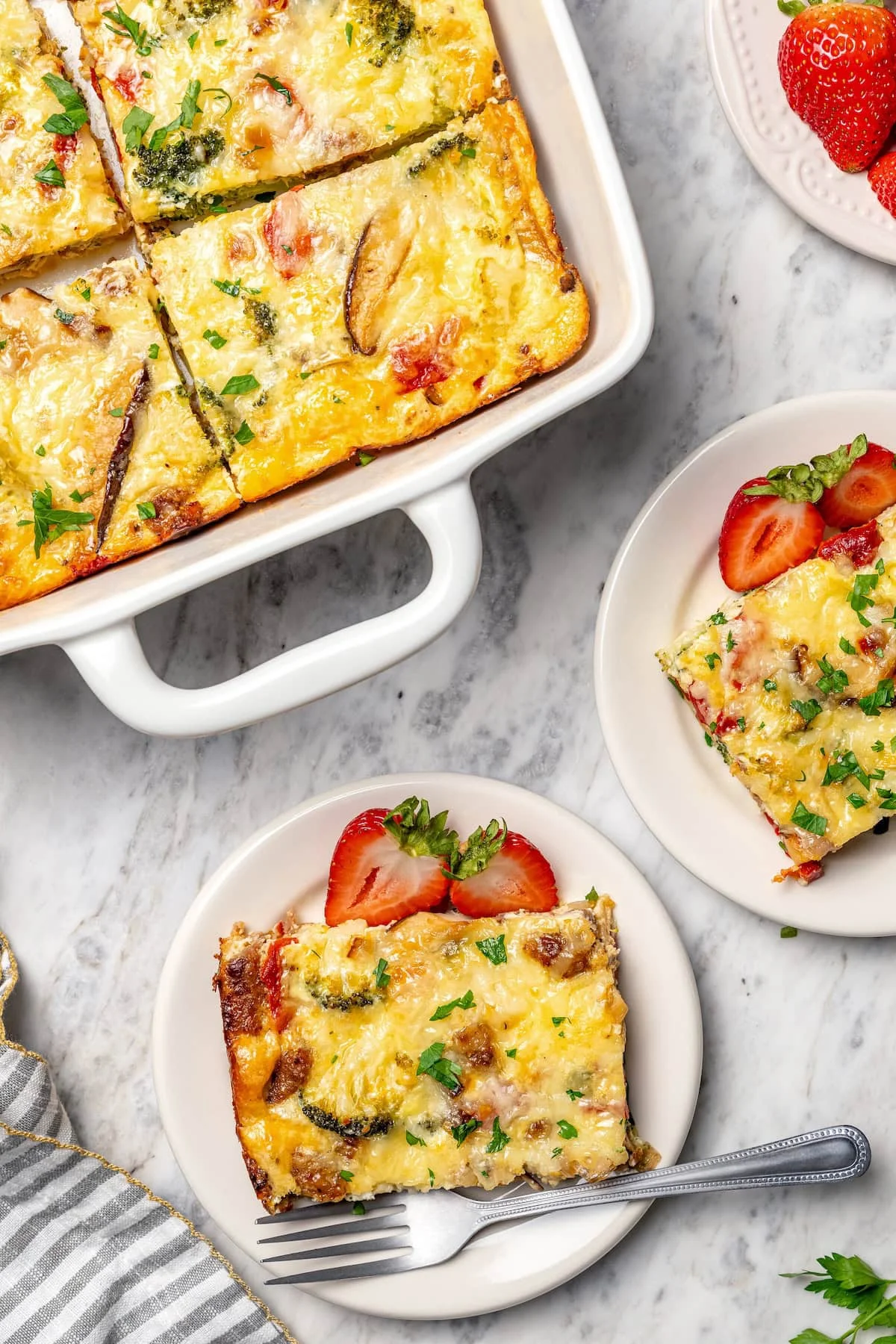Two plates of breakfast casserole set next to baking dish.