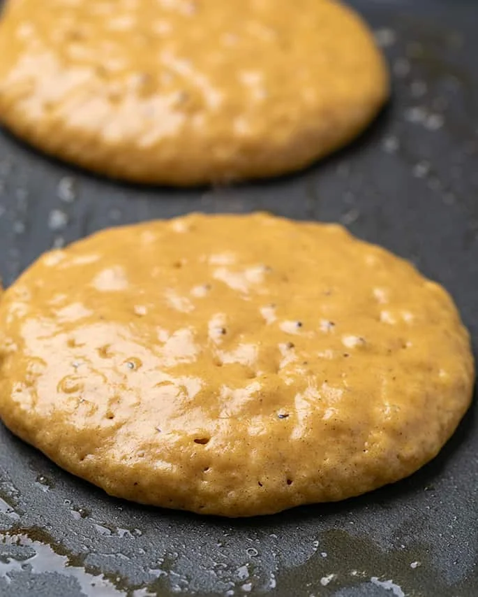 Two raw but nearly set pumpkin pancakes on black griddle with butter