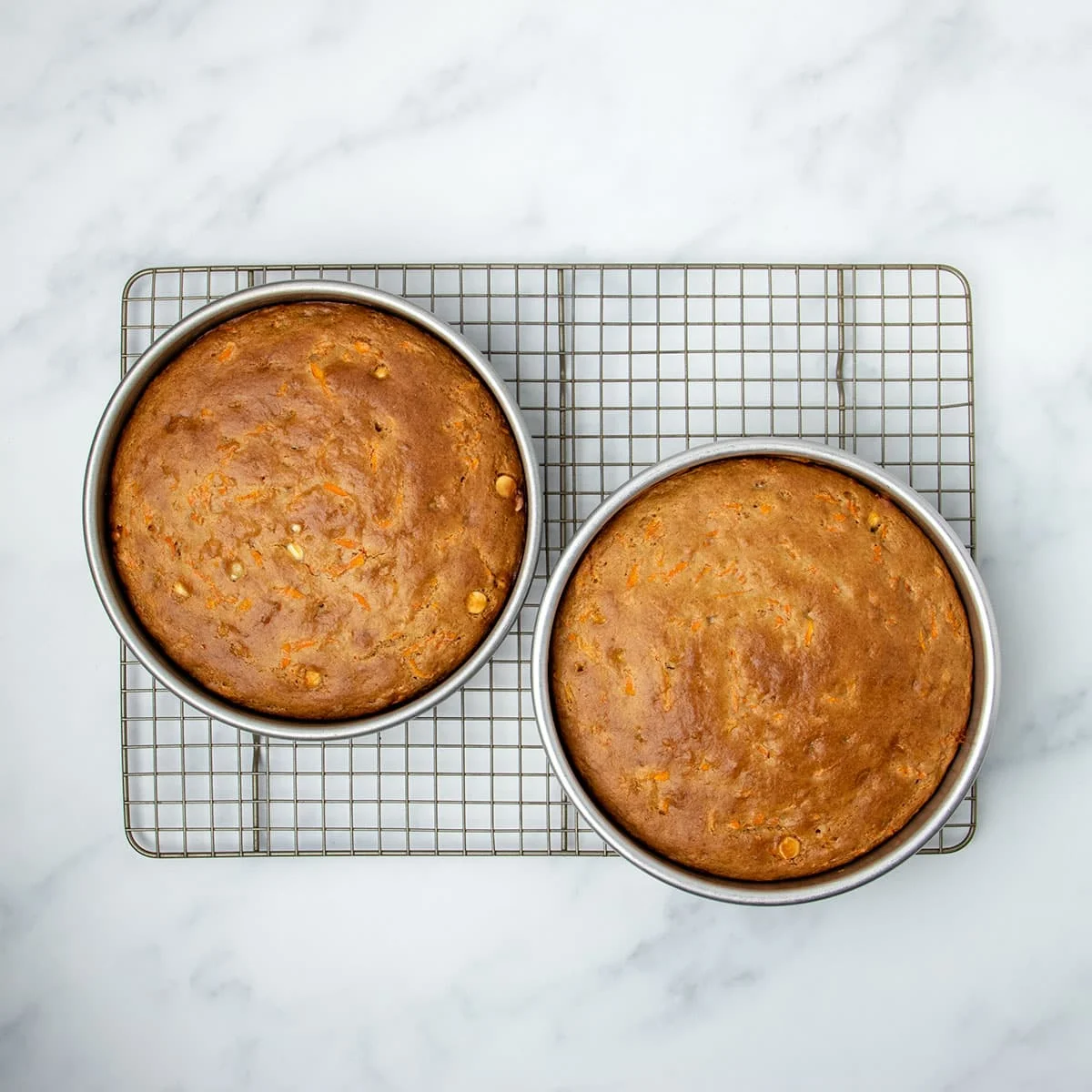 Two round cake pans with baked browned cake on wire rack.