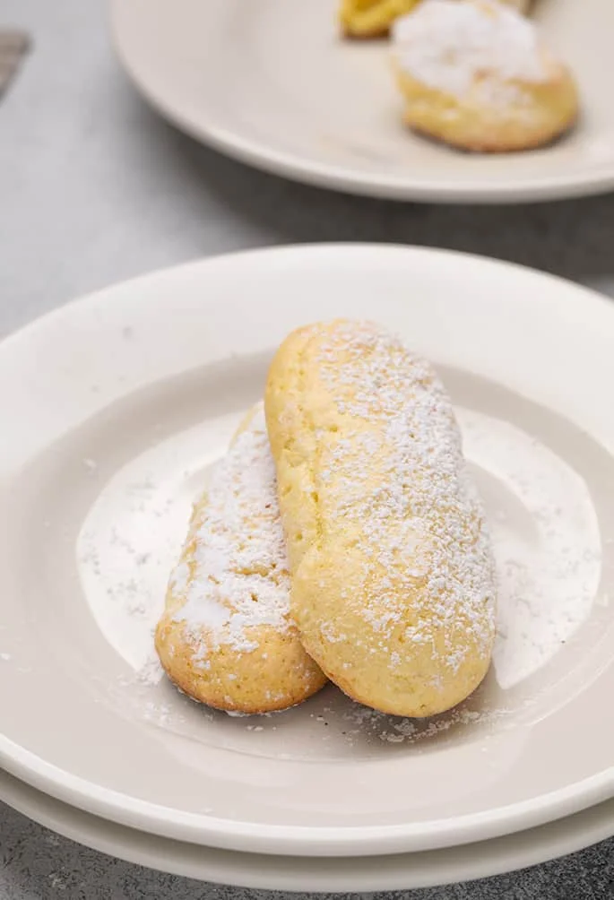 Two whole ladyfingers on a stack of 2 small white plates