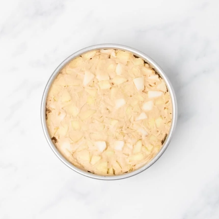 Unbaked cake batter with visible apple pieces spread in a round pan.