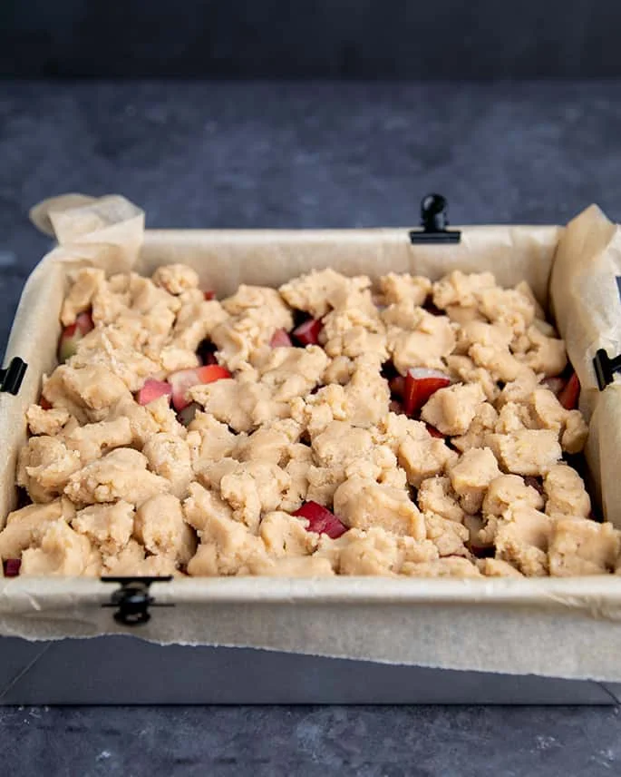 Unbaked crumble topping on top of strawberries and rhubarb in metal square pan
