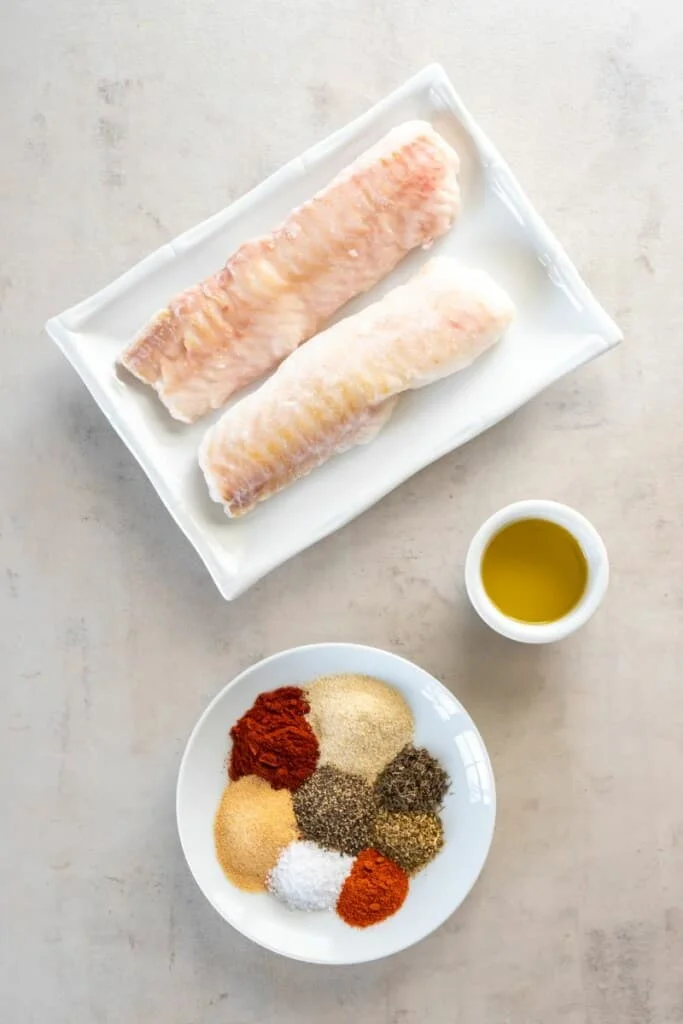 Uncooked cod on a white plate, spices & seasonings on a separate white plate.