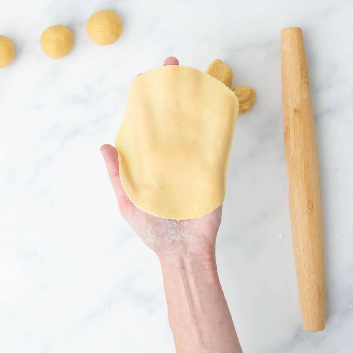 Uncooked tortilla held in hand, showing its flexibility and thinness.