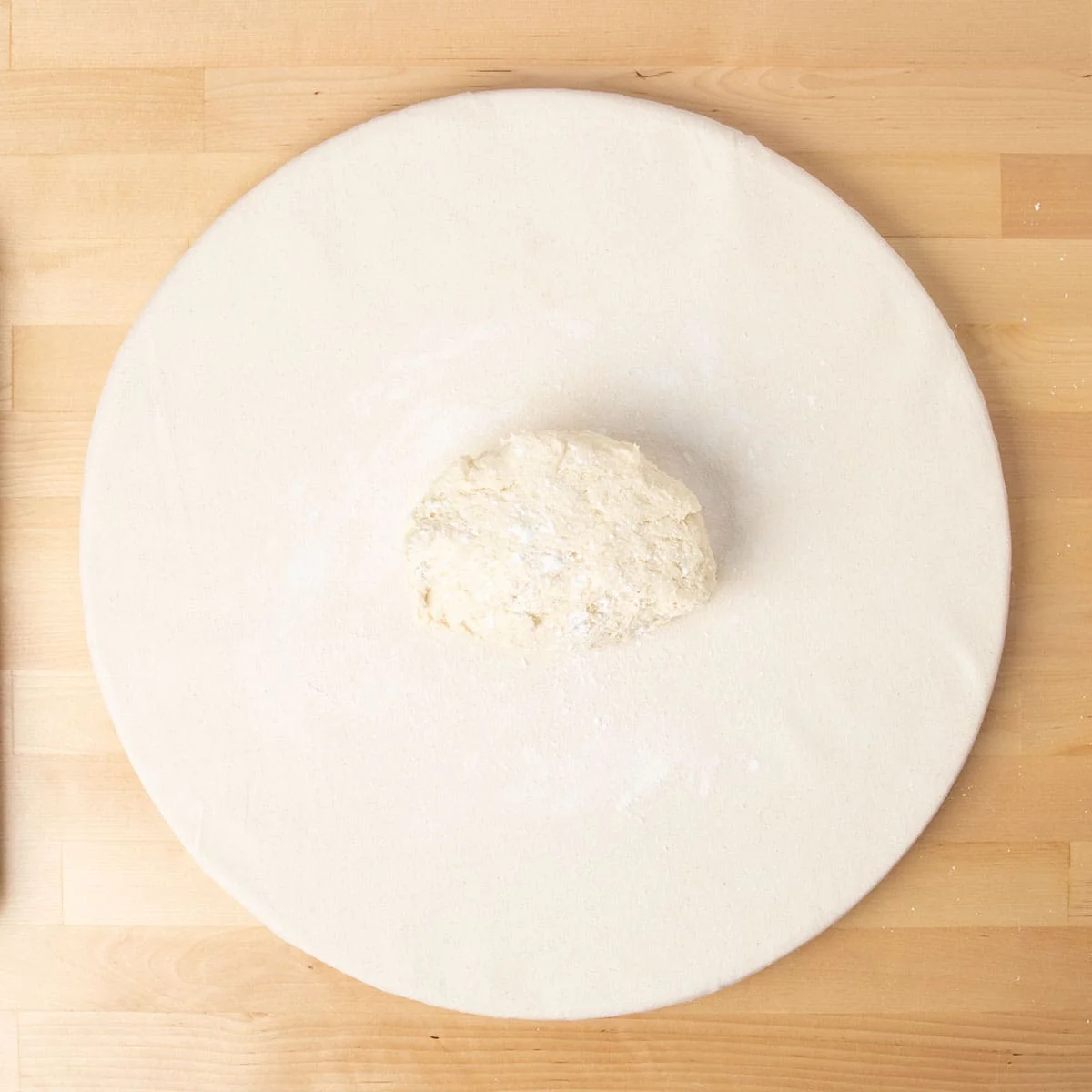 unshaped half raw gluten free donut dough from bucket on white surface with sprinkled flour