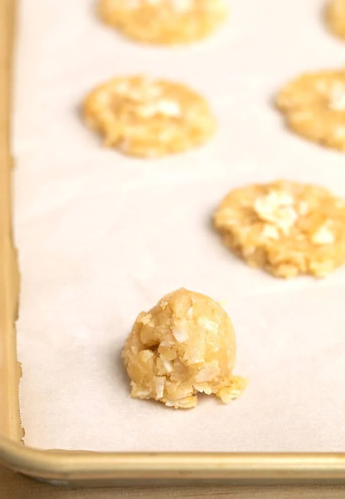 Unshaped scoop of coconut chip cookie dough on white paper on tray