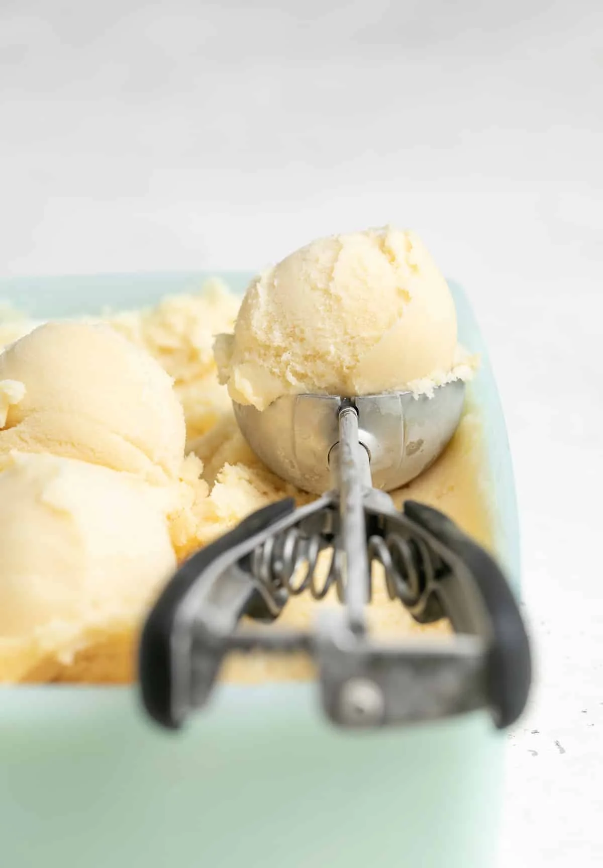 Vanilla ice cream in an ice cream scoop in a green freezer container with more ice cream