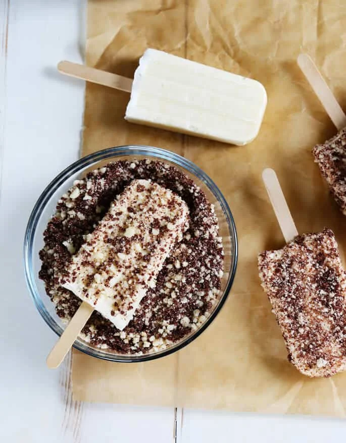 Vanilla ice pops being dipped in chocolate eclair crumbs 