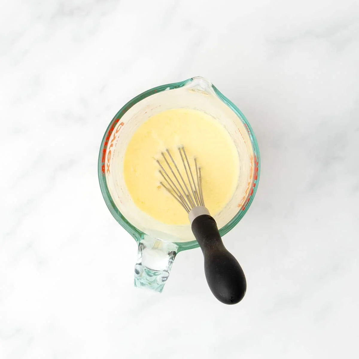 Wet ingredients whisked together in a glass measuring cup to form a smooth, pale yellow mixture.