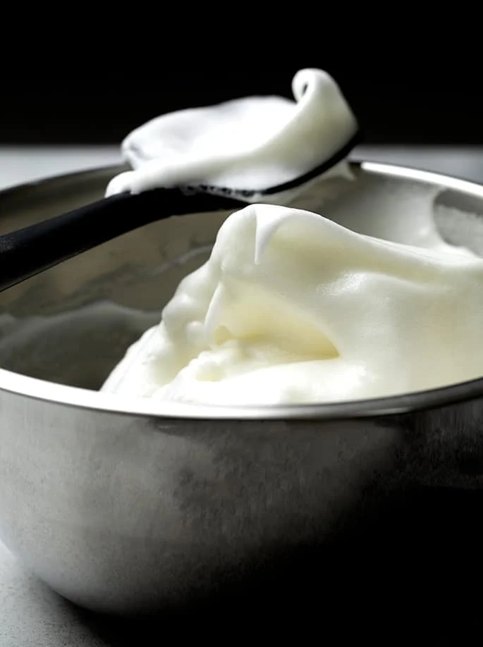 Whipped egg whites in peaks in metal bowl with black spatula