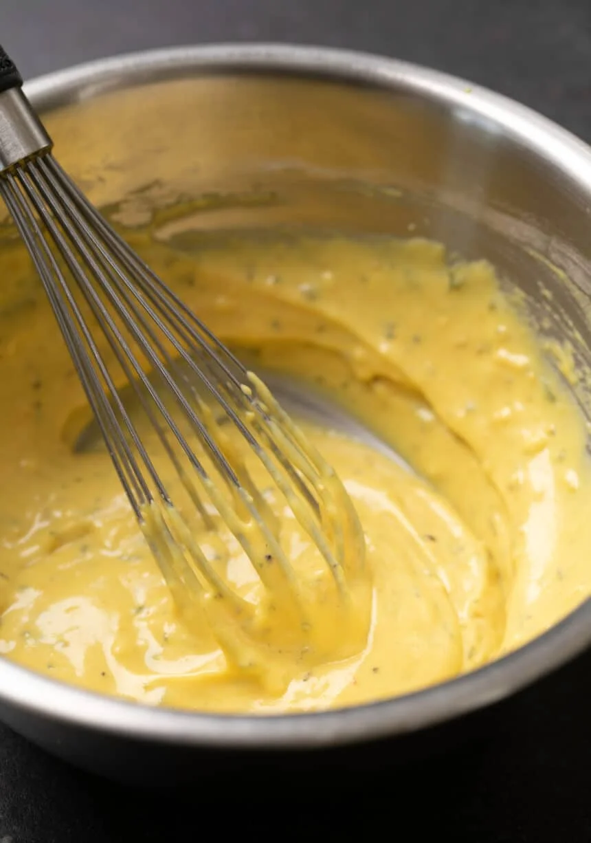 Whisk in yellow batter with flecks of green in round metal bowl