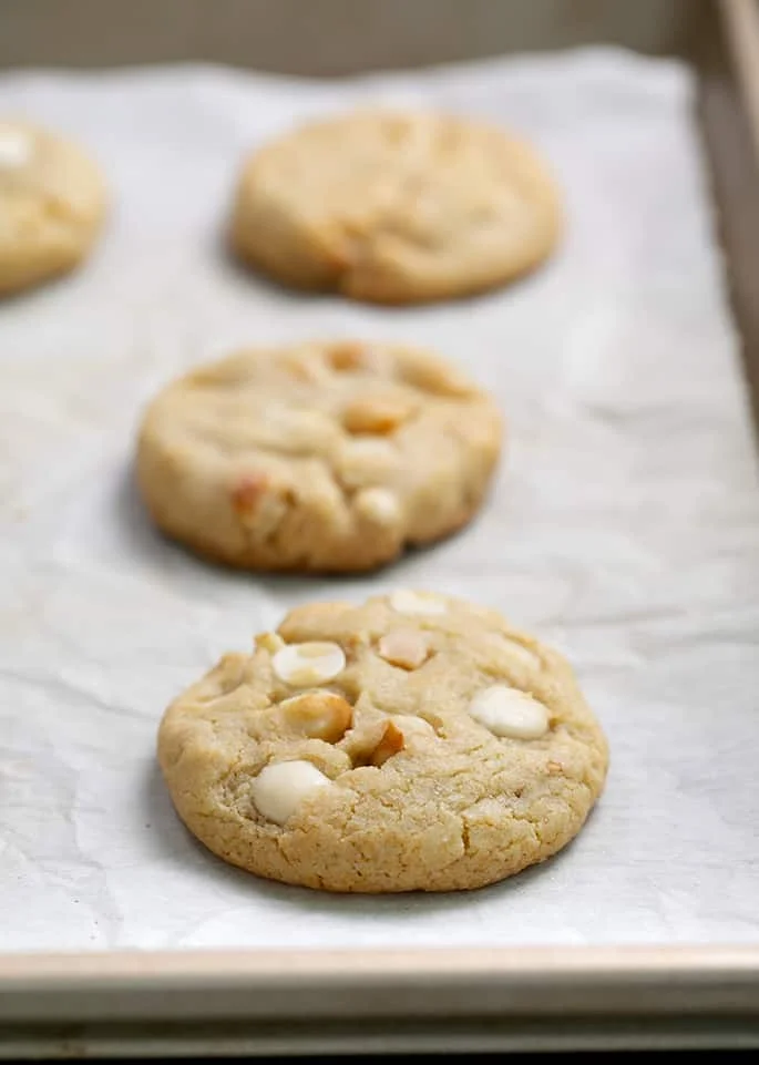 White chocolate macadamia cookies baked on white paper on tray.