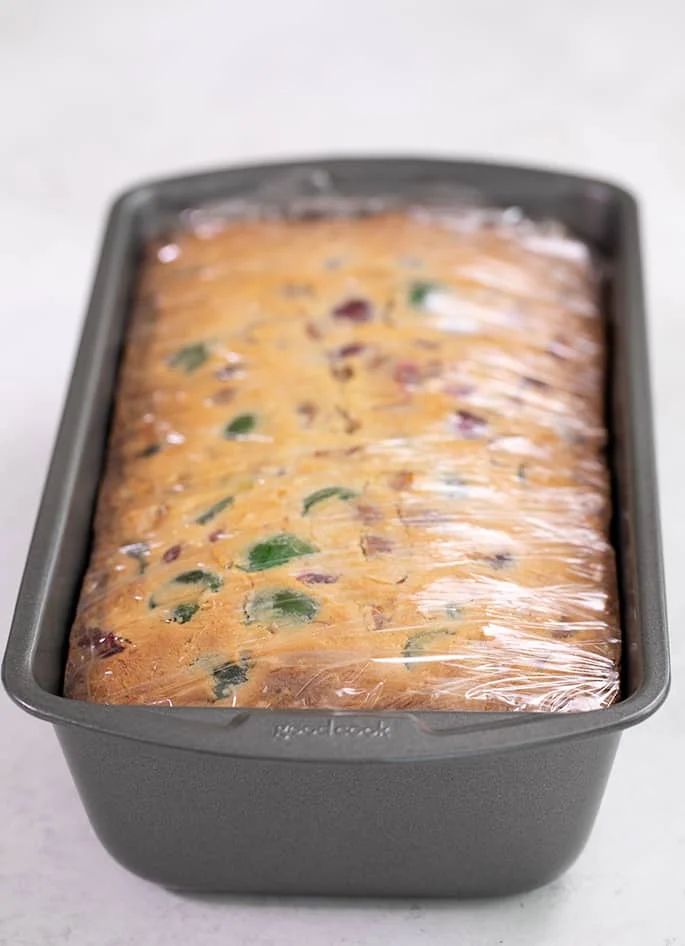 White fruit cake soaked in syrup wrapped in plastic in loaf pan
