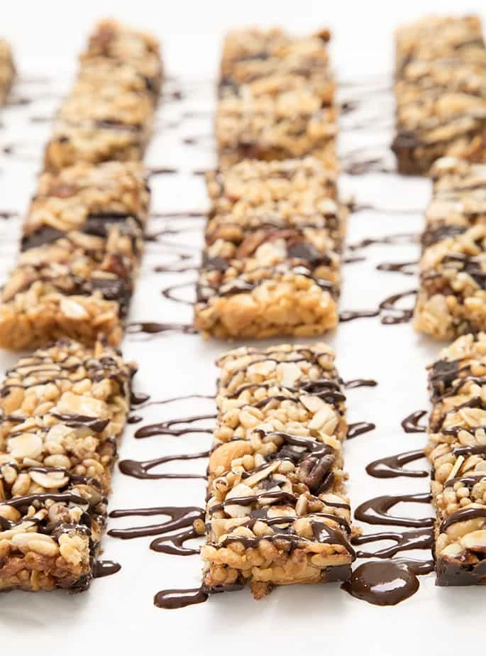 White paper with light brown homemade cereal bars with a melted chocolate drizzle