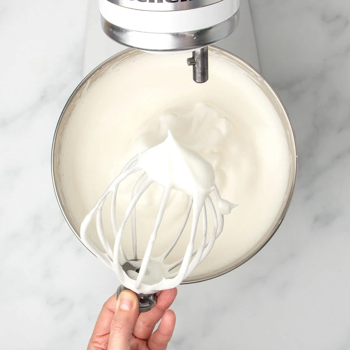 white raw meringue in mixing bowl with stiff peaks of meringue on wire whisk