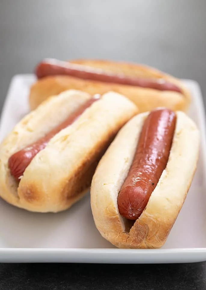 White rectangular plate with 3 hot dogs in buns.