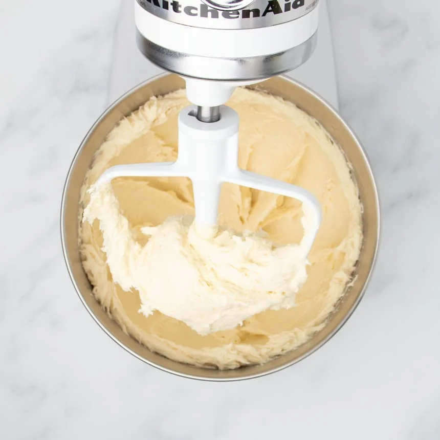 white stand mixer paddle attachment with very soft pale batter on paddle and in bowl below it
