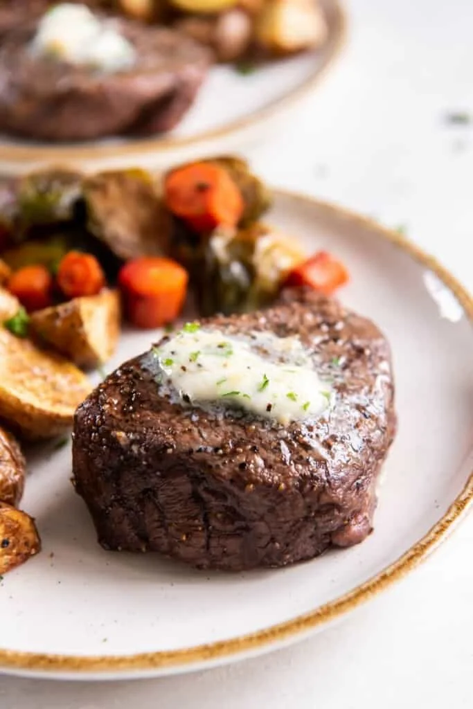Whole air fried filet mignon with melted butter on a white plate with mixed vegetables.