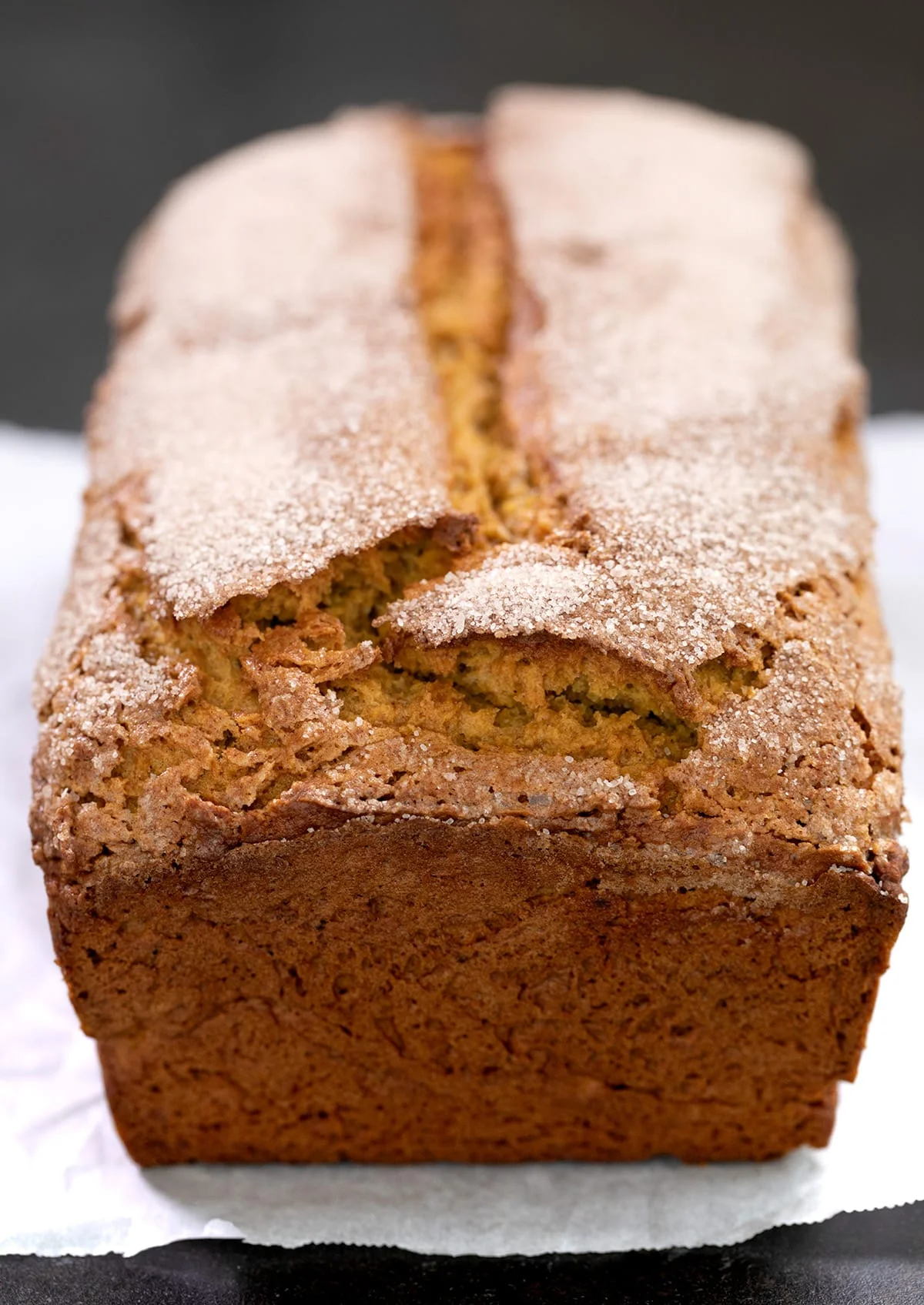 Whole baked gluten free pumpkin bread with cinnamon sugar on top sitting on white paper