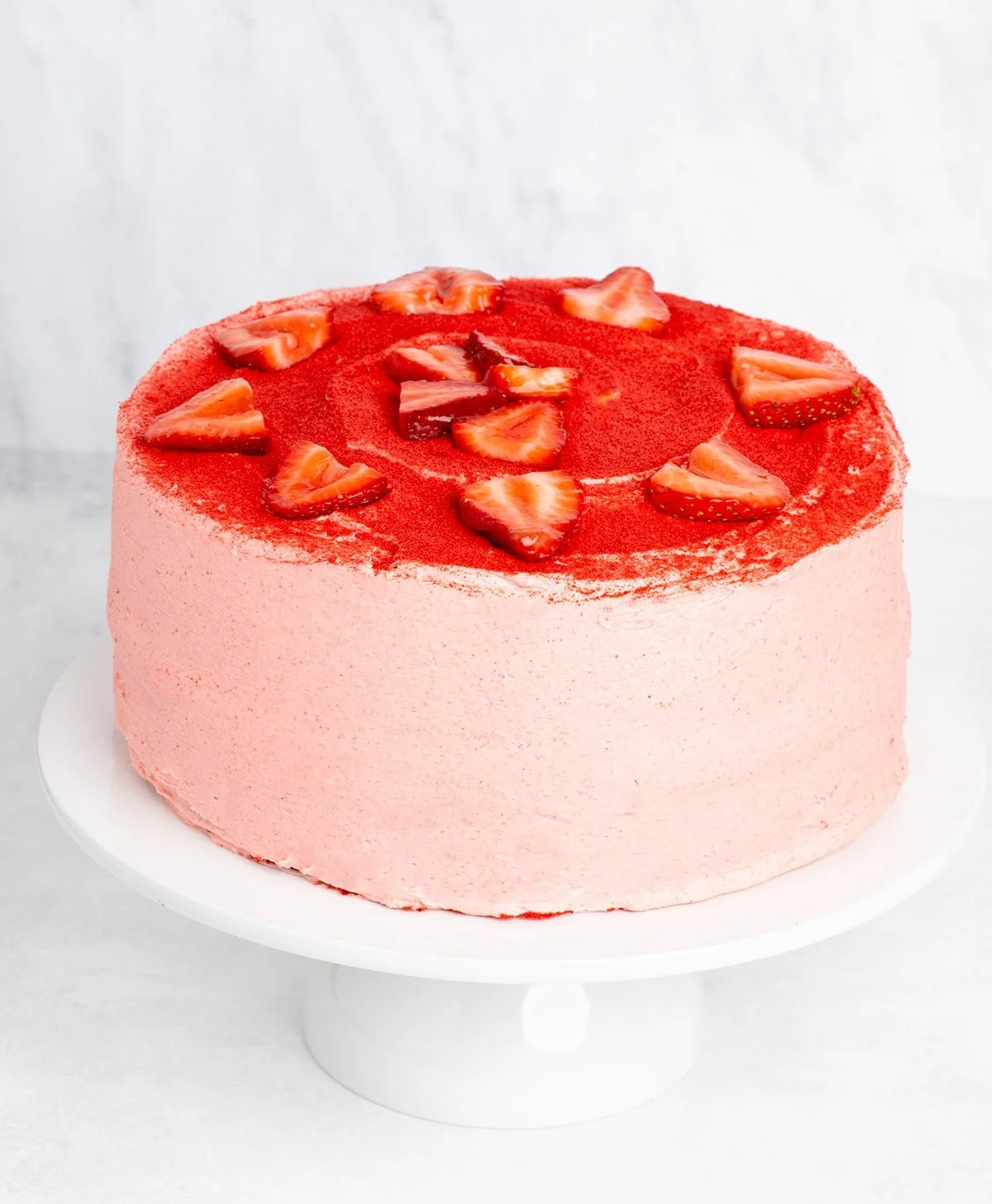 Whole cake covered in pink frosting and red powder, decorated with strawberry slices on top.