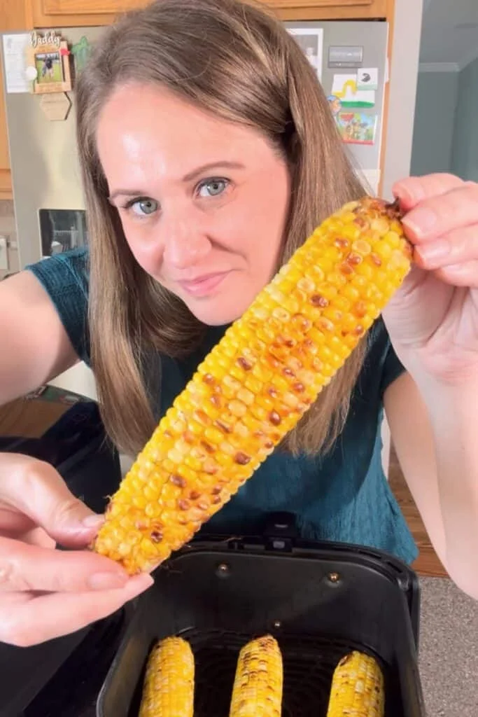 Woman (me) holding a piece of air fryer corn on the cob with hands toward the camera to see the roasted spots.