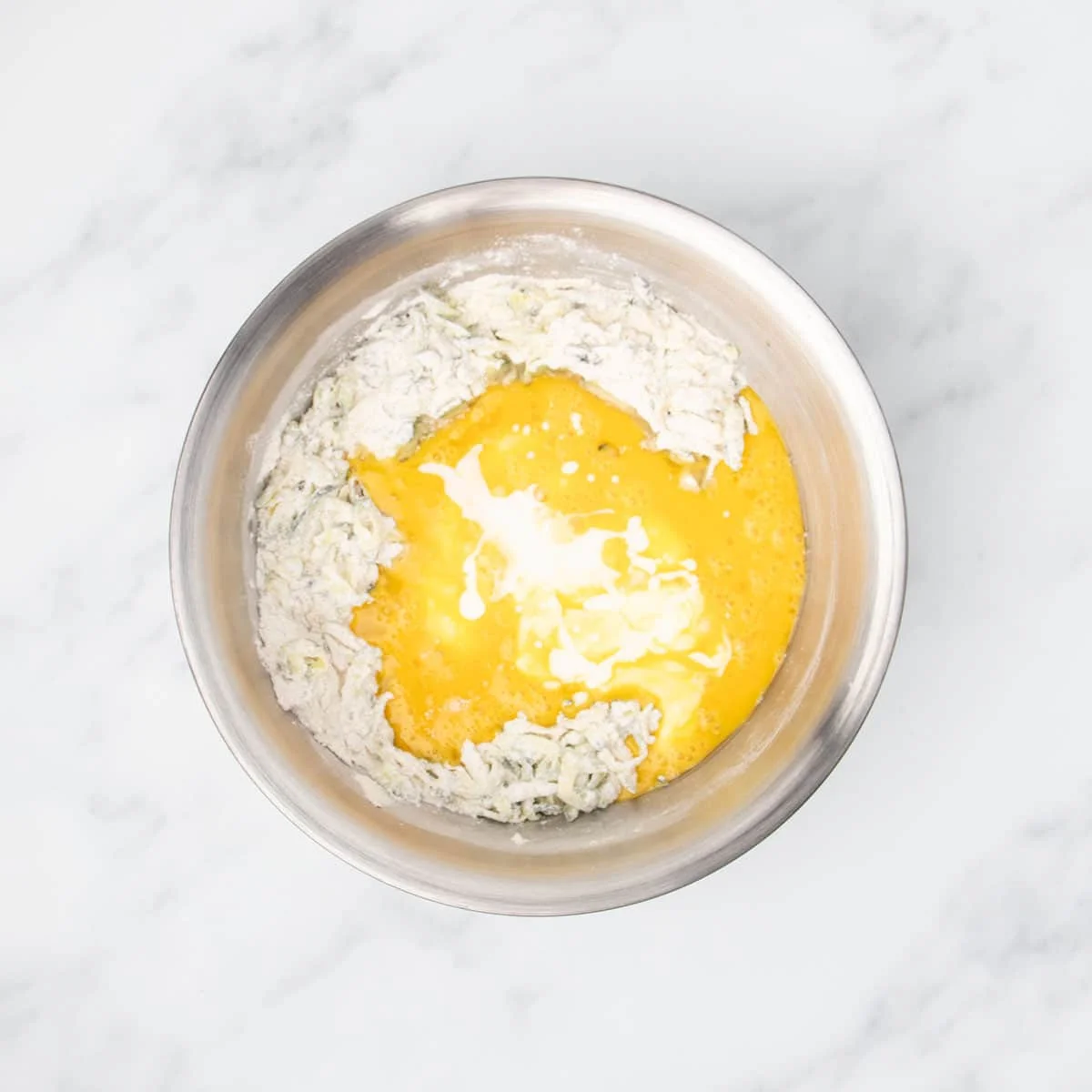Yellow beaten eggs and white buttermilk on top of flour mixture in mixing bowl.